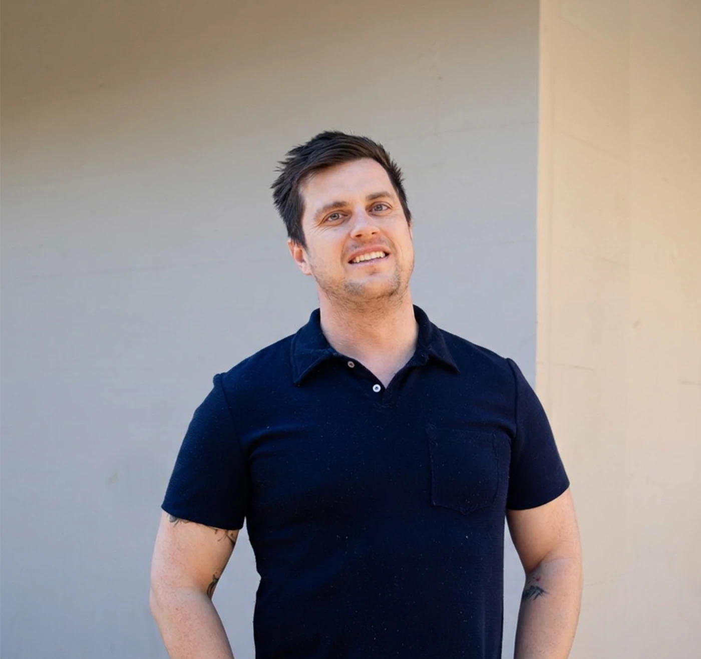 Brendan Smith, finance broker at Tenon Finance, in a navy polo shirt, smiling, standing against a plain sunlit wall