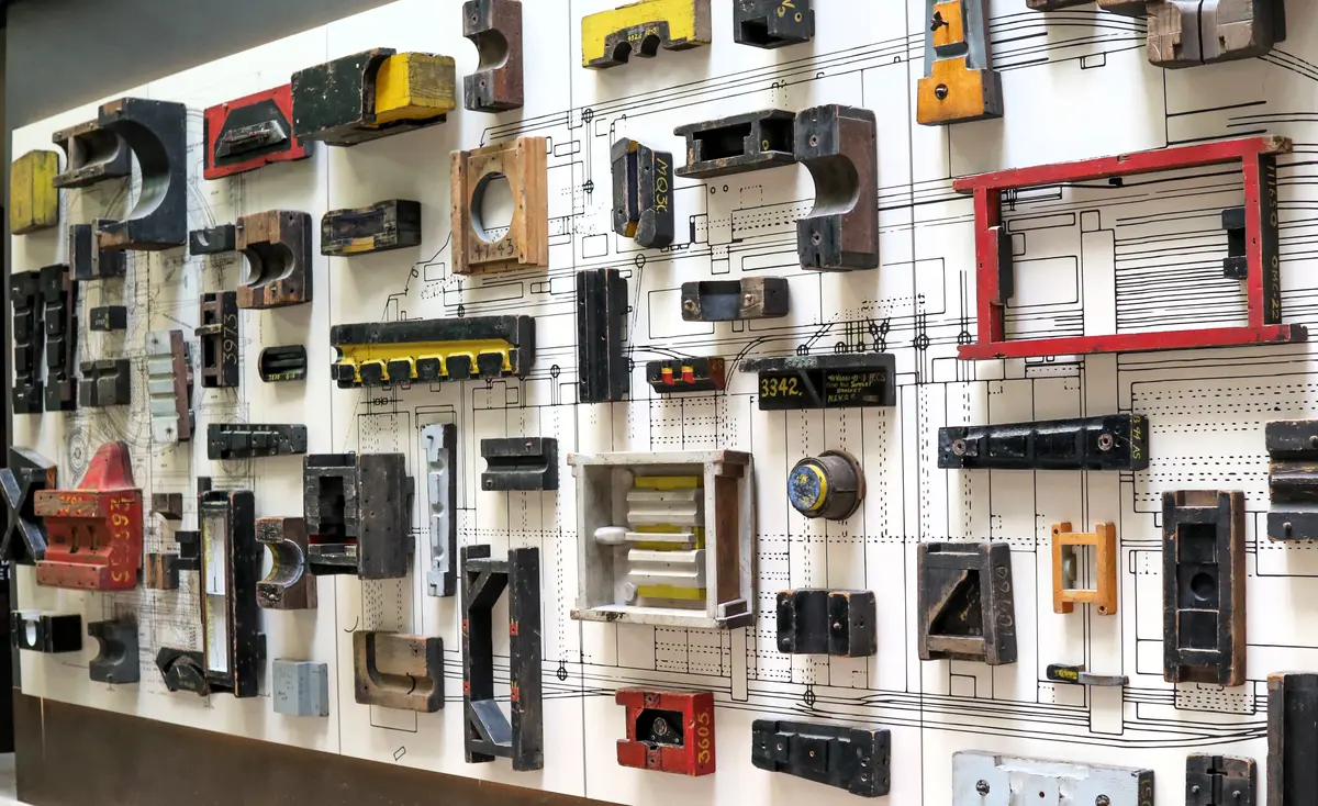A wall of old wooden foundry patterns in black, red and yellow, mounted over a large technical drawing