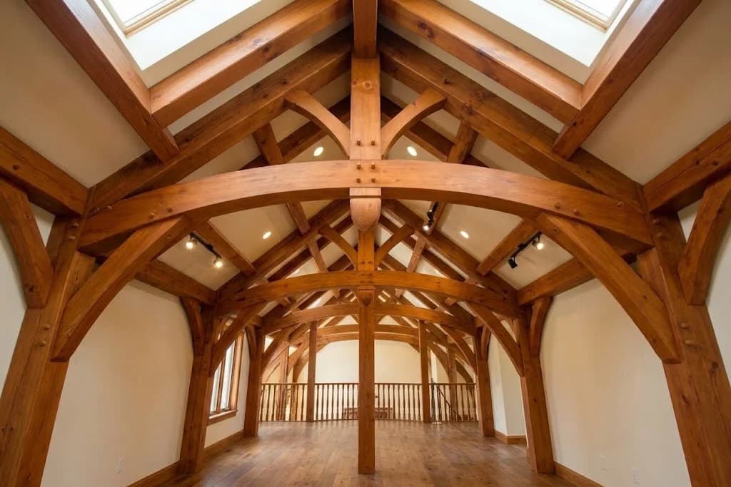 A timber frame interior under a pitched roof: curved timber braces pegged into posts and rafters form a row of arches down the length of the room